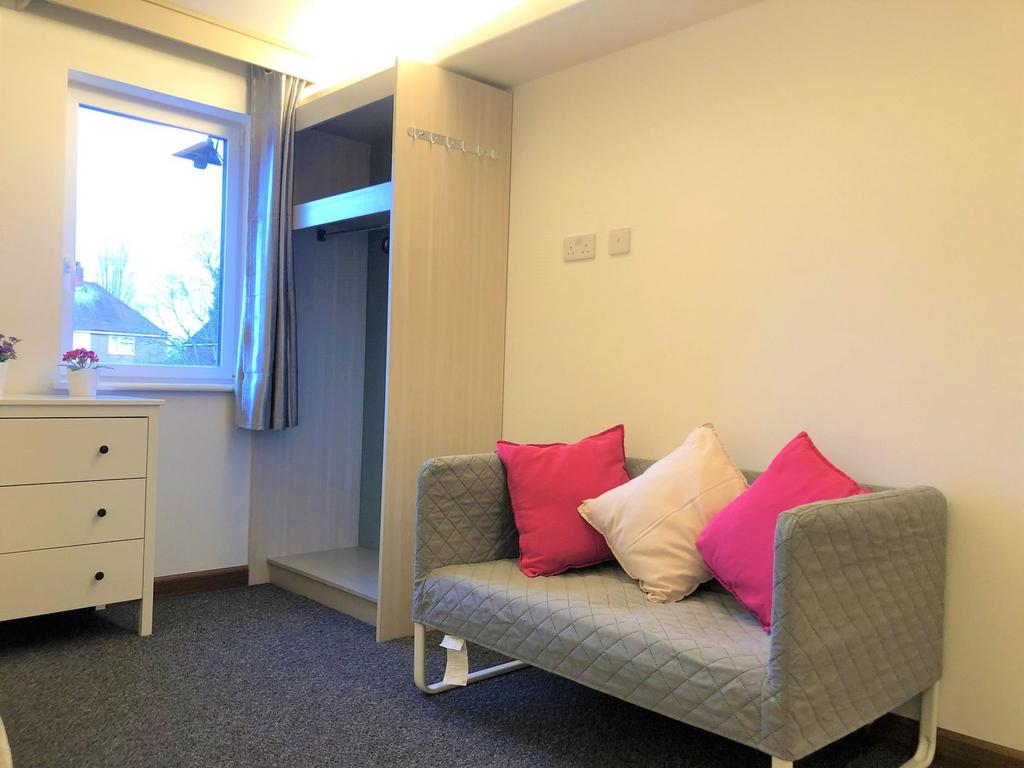 A cozy single bedroom featuring a neat gray sof...