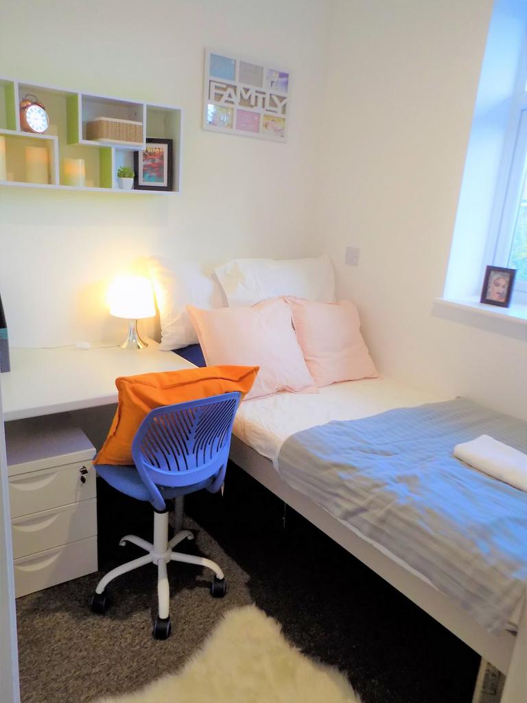 Bright, neatly arranged single bedroom with a c...