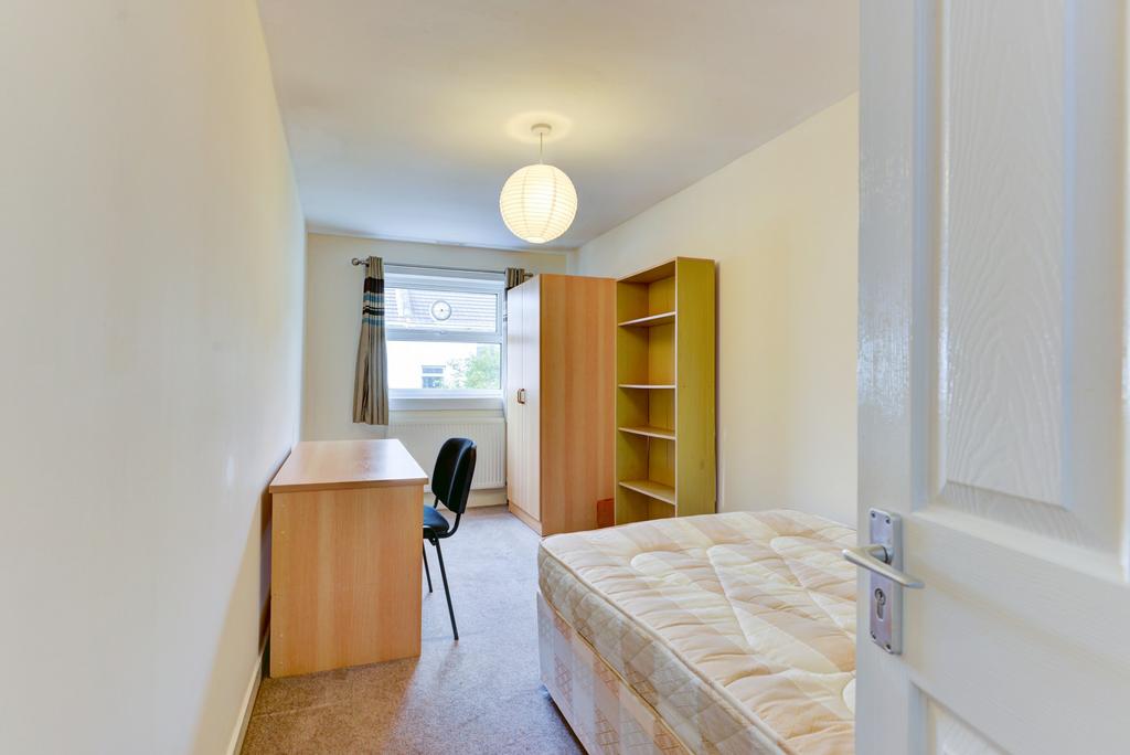 A tidy bedroom featuring a single bed, a desk w...