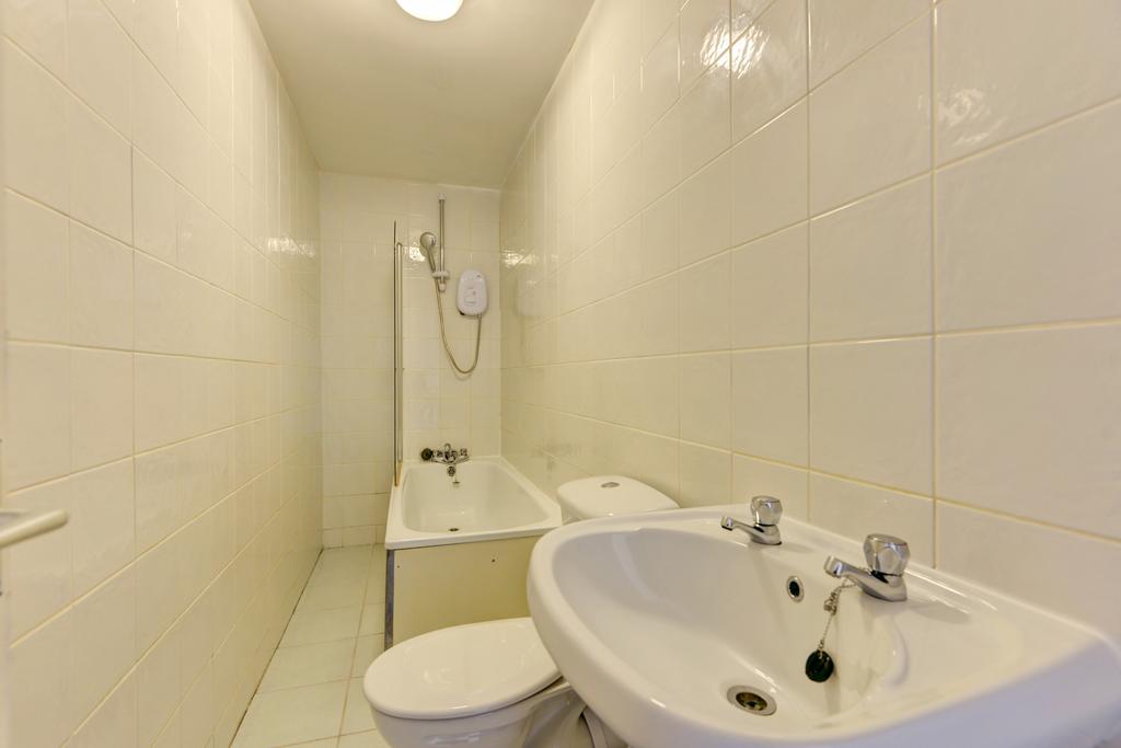 Compact tiled bathroom with a bathtub and overh...
