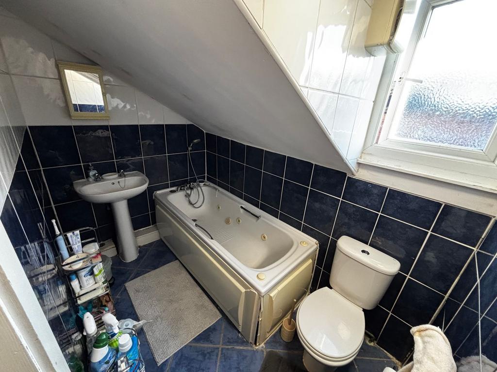 Compact tiled bathroom with a bathtub under a s...