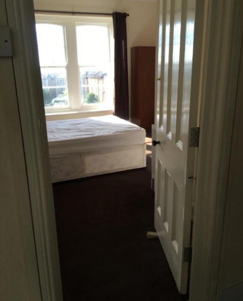 A double bedroom with a bed frame and large win...