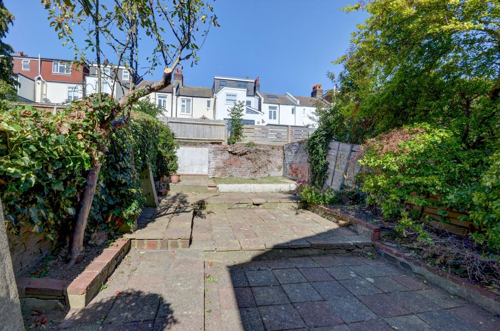 Sunny paved rear garden with terraced planting ...