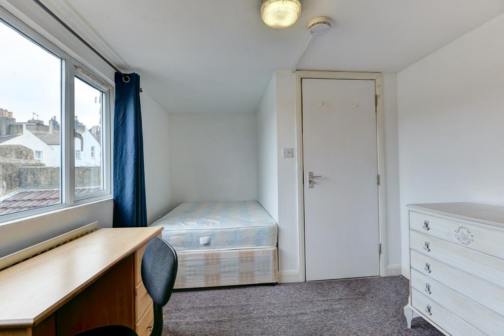 A well-lit, tidy single bedroom featuring a bed...