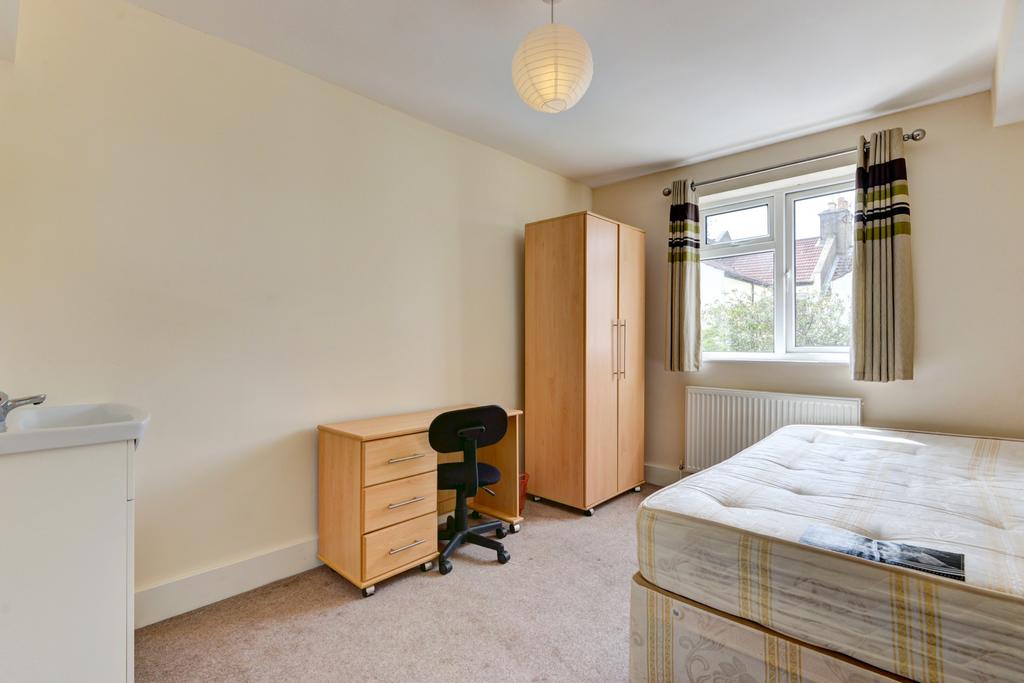 A well-lit, tidy bedroom with a single bed, a w...
