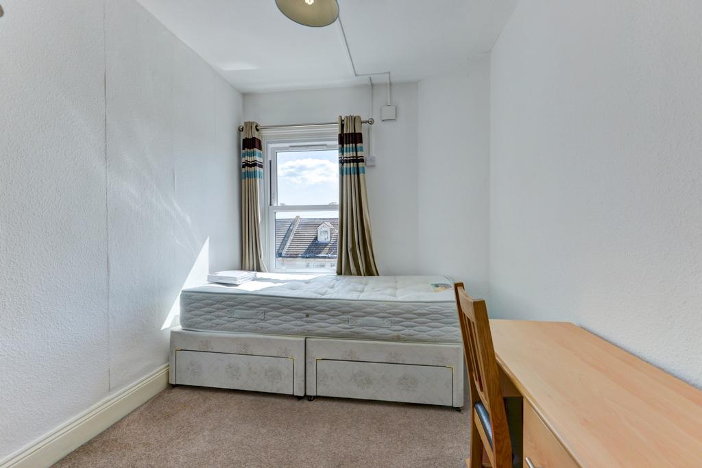 A tidy single bedroom with a well-made bed posi...