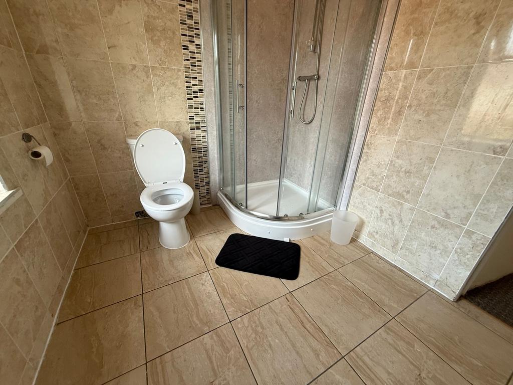 Bright, tiled bathroom with a corner glass show...