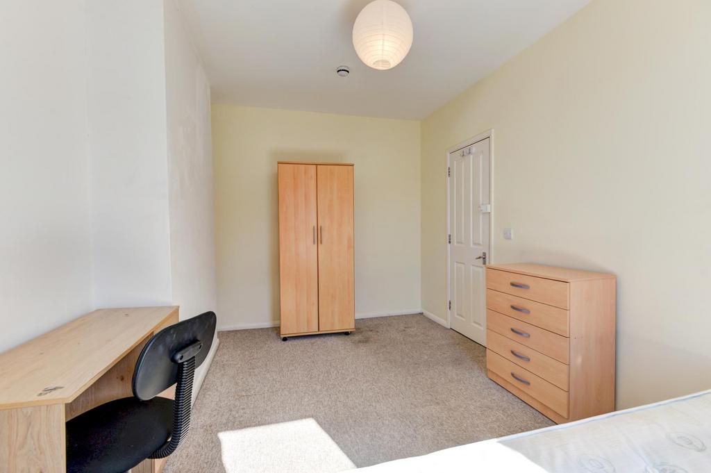 A well-lit bedroom with a desk, a wardrobe, and...