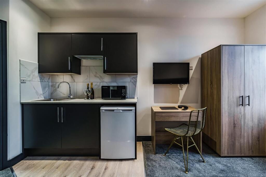 Modern studio kitchenette with dark cabinets, c...