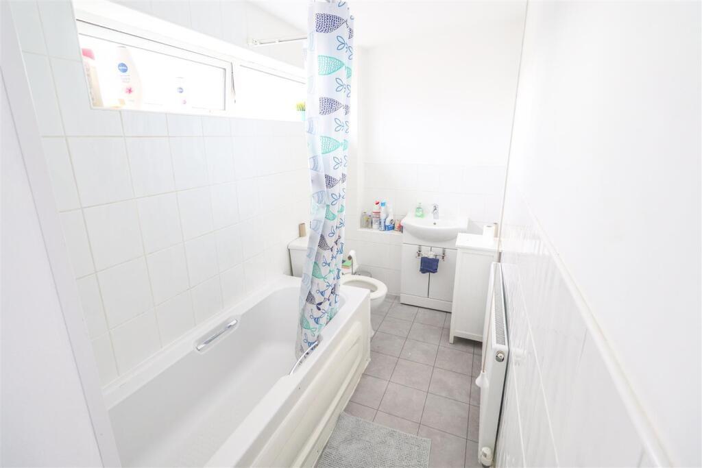 Bright, clean bathroom with a white bathtub, sh...