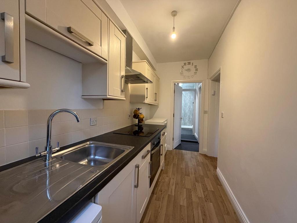 Bright galley kitchen with white cabinetry, a s...