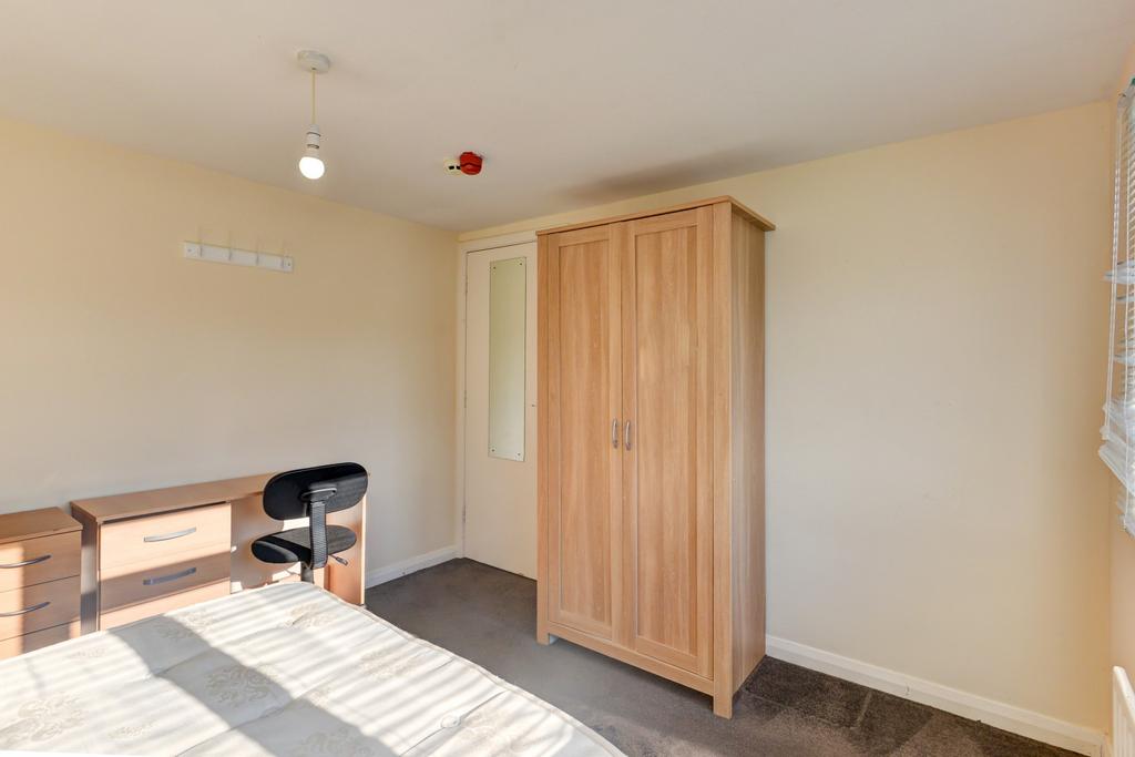 A neat and modest bedroom featuring a bed, a wo...