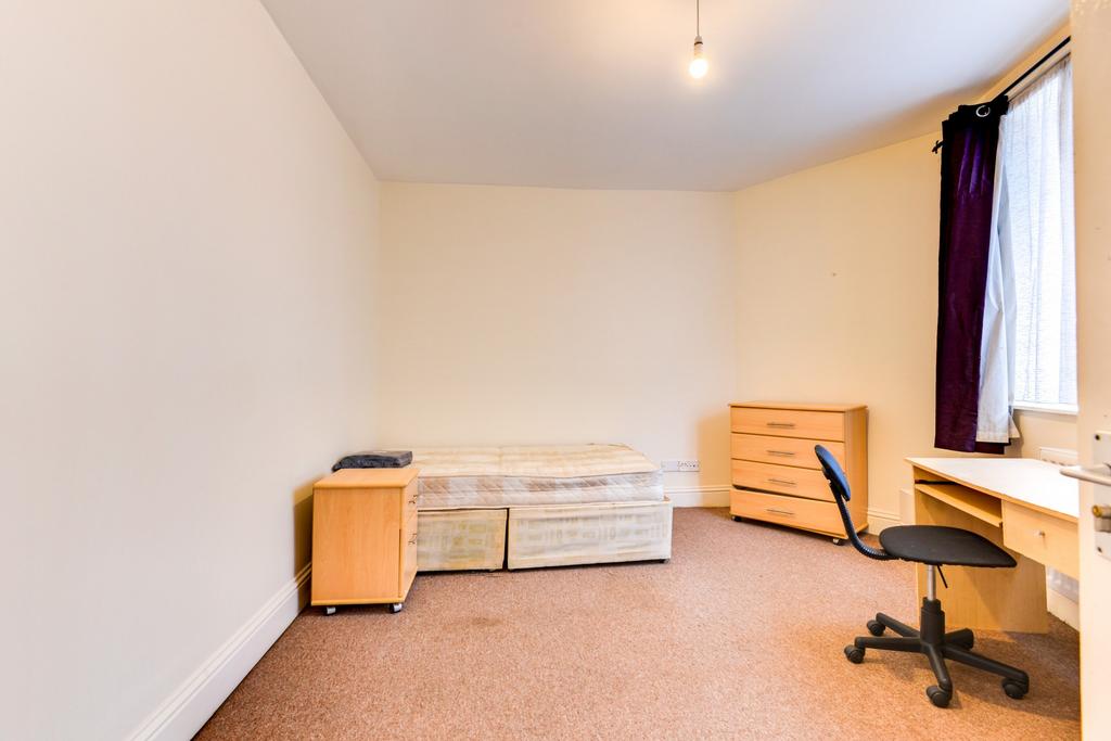 A simple bedroom with a single bed, a desk and ...