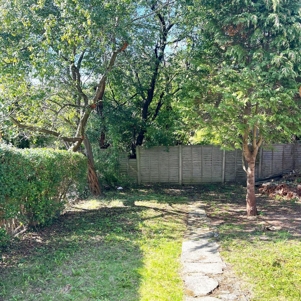 Sunny private garden with mature trees, a paved...