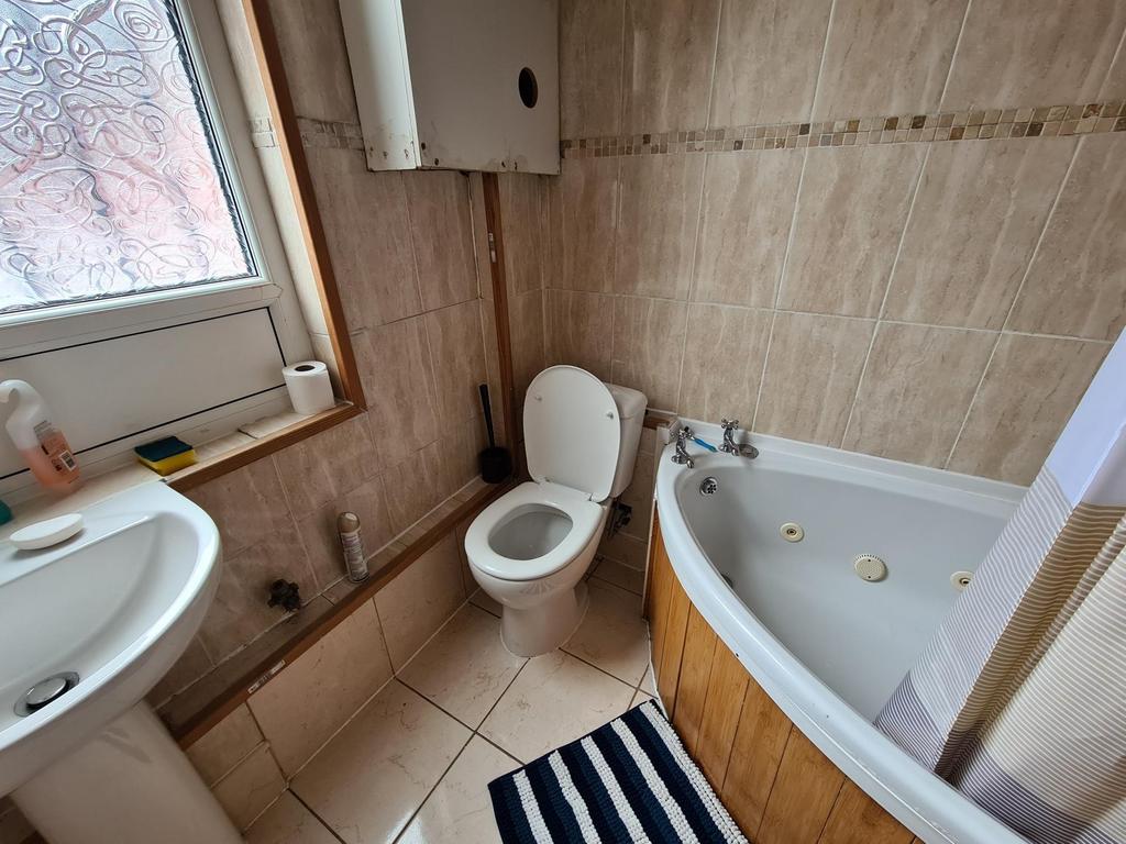 Bright tiled bathroom with a corner bath, pedes...