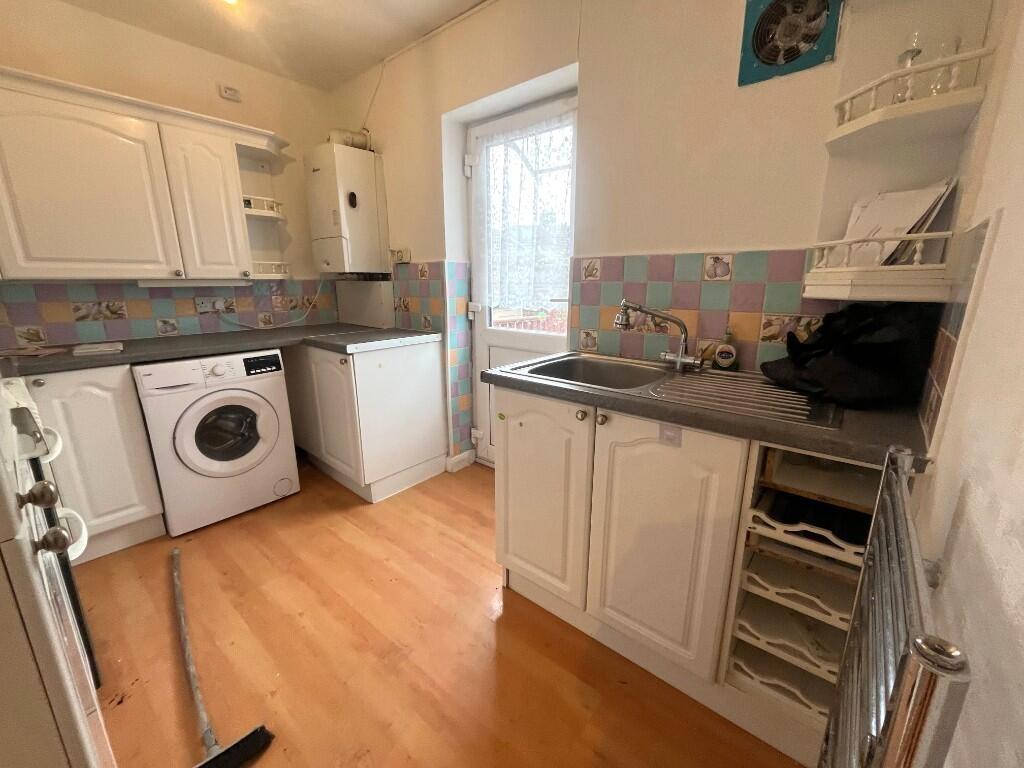 Bright compact kitchen with white cabinetry, wo...