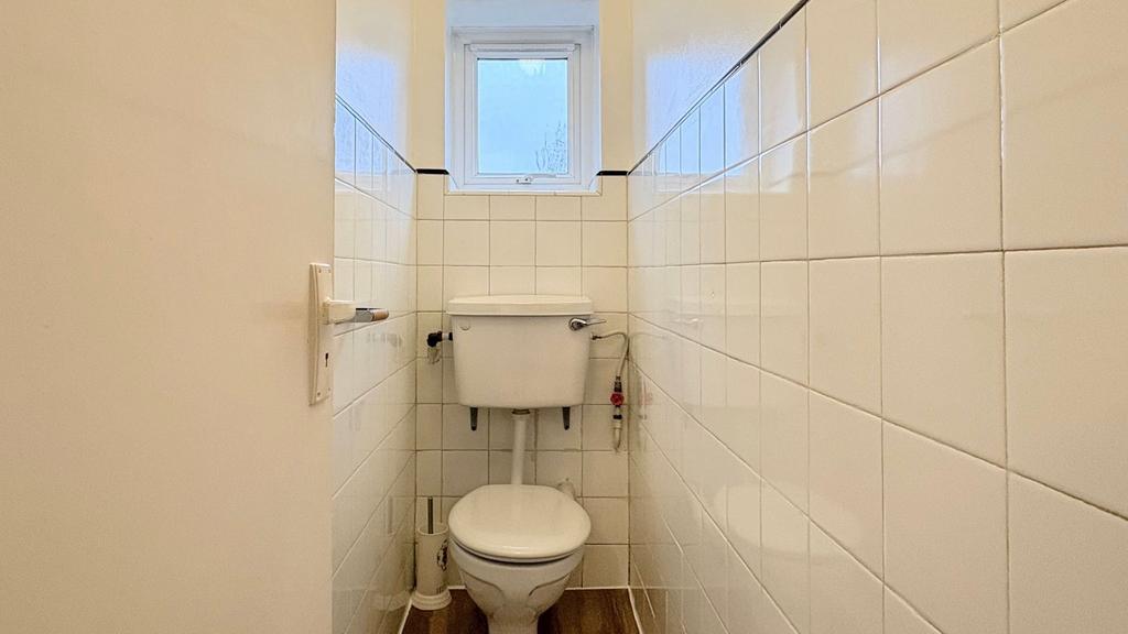 Compact, bright WC with white tiled walls, a hi...