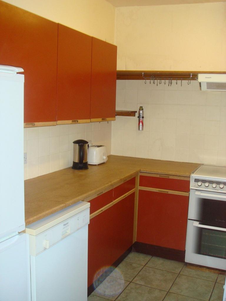 A compact, functional kitchen with warm red cab...