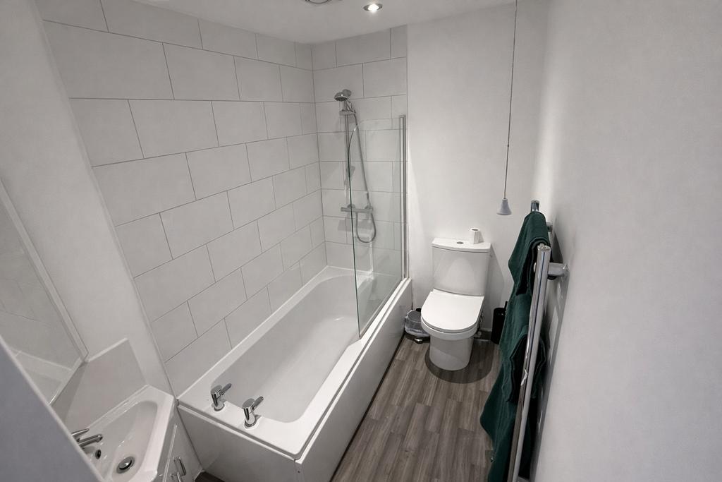 Bright, modern bathroom with tiled bath and sho...
