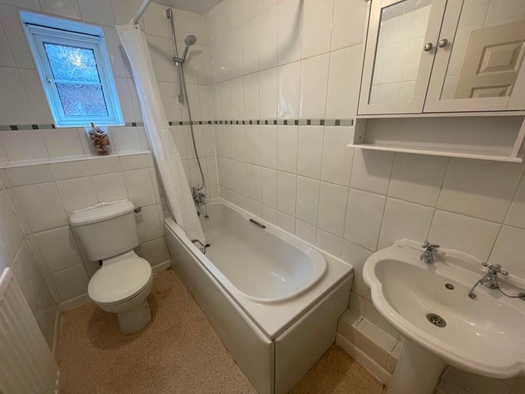 Bright, neatly tiled bathroom with a bathtub an...