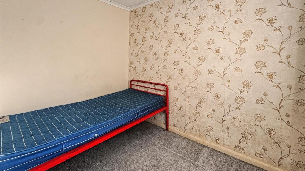 Simple bedroom with bed and patterned wallpaper...