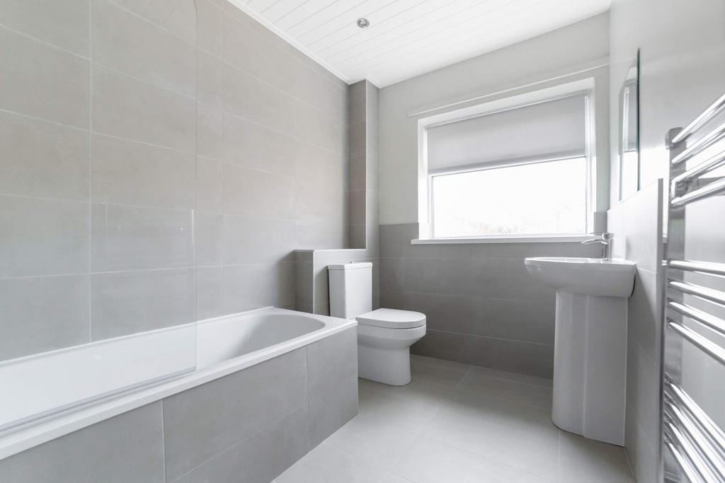 Modern tiled bathroom with bath and bright wind...
