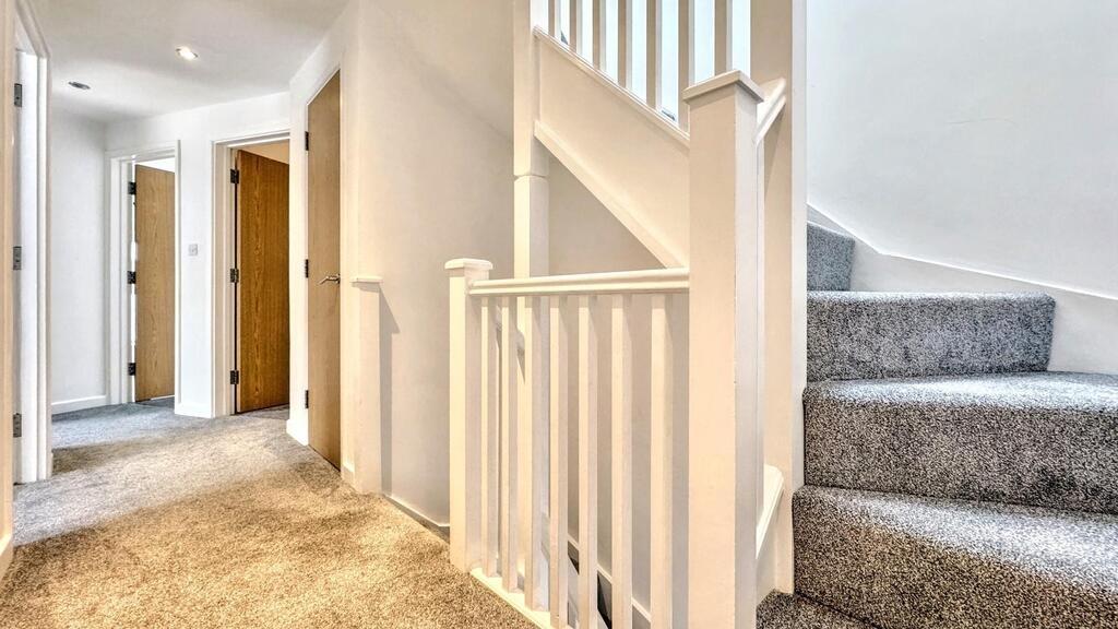 Bright carpeted hallway with staircase and door...