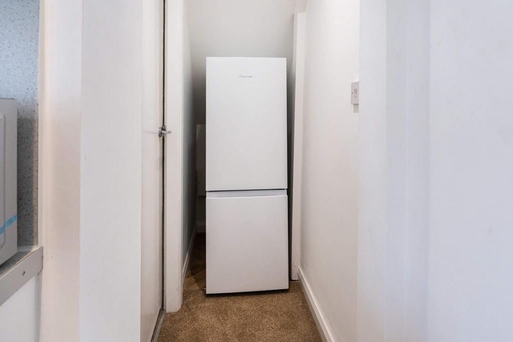 Narrow kitchen corridor with freestanding fridg...
