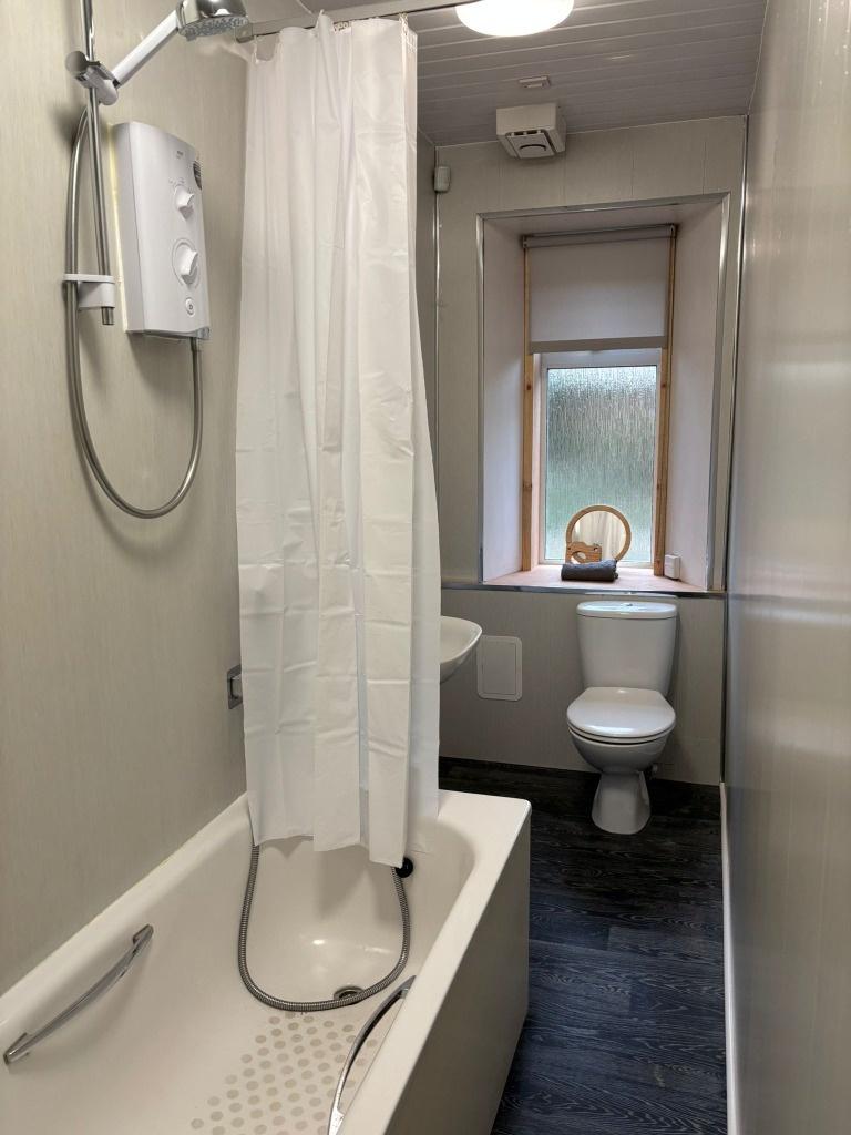 Compact bathroom with shower-over-bath and wind...
