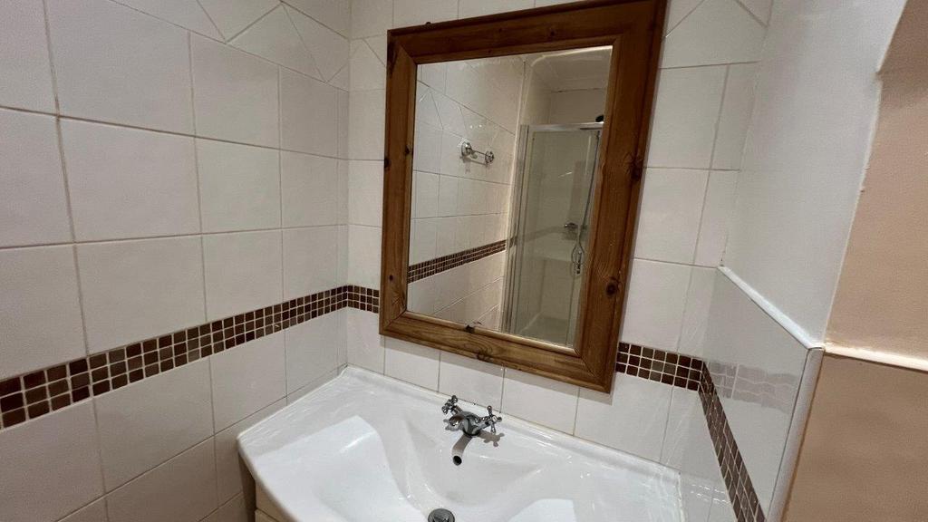 Tiled bathroom sink with framed mirror and show...